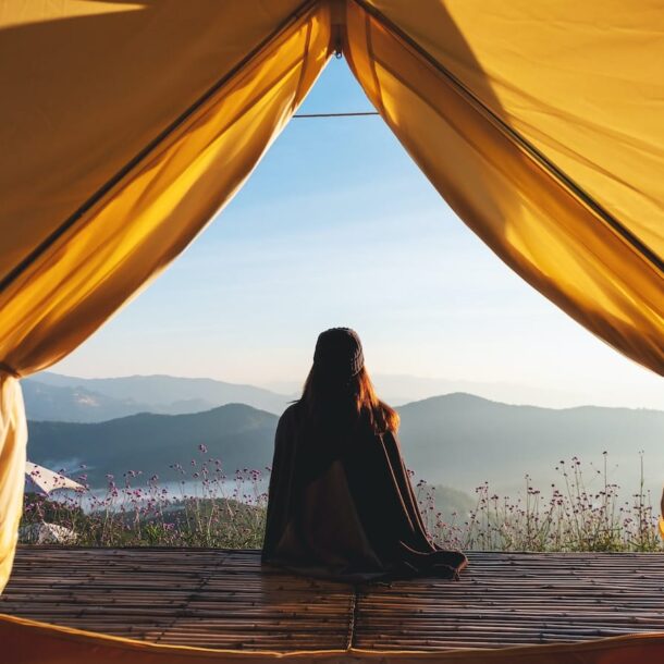 A person sitting at the entrance of a tent overlooking a mountain vista, suggesting considering the location when learning how to choose the right resort.
